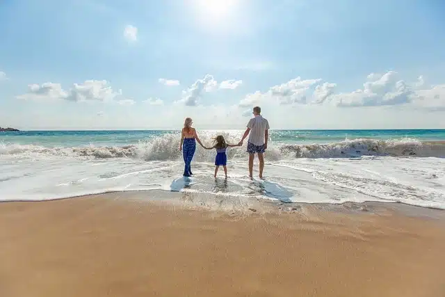Family holding hands on the beach at sunset with arms outstretched.