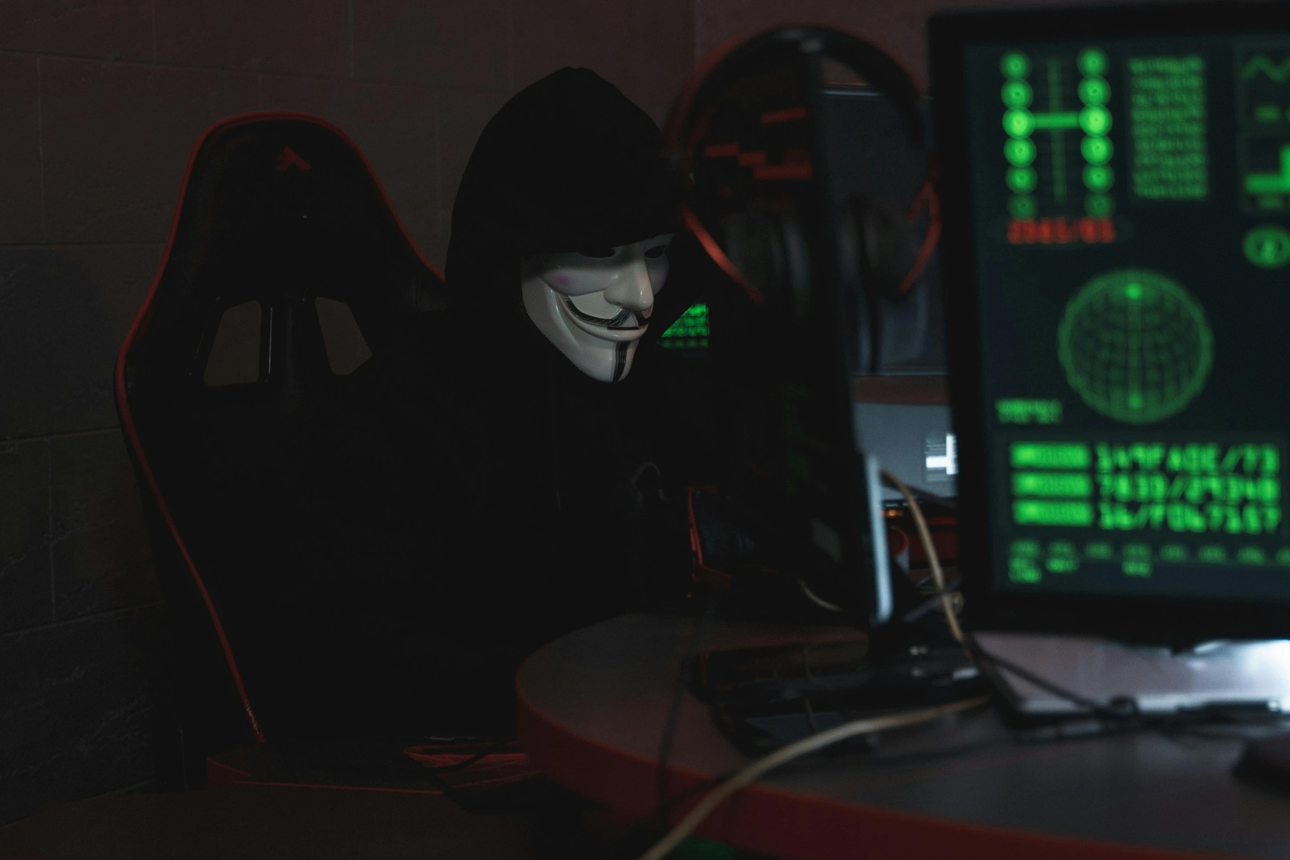 Kapucnis ruhás hacker számítógép előtt, zöld kódok a háttérben