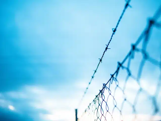 Barbed wire fence against blue sky, symbolic representation of border protection.