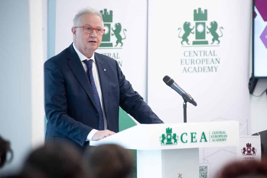 Előadó férfi prezentál a CEA pódiumán, háttérben kivetítővel