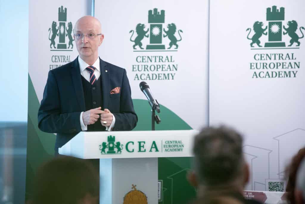 Előadó férfi prezentál a CEA pódiumán, háttérben kivetítővel