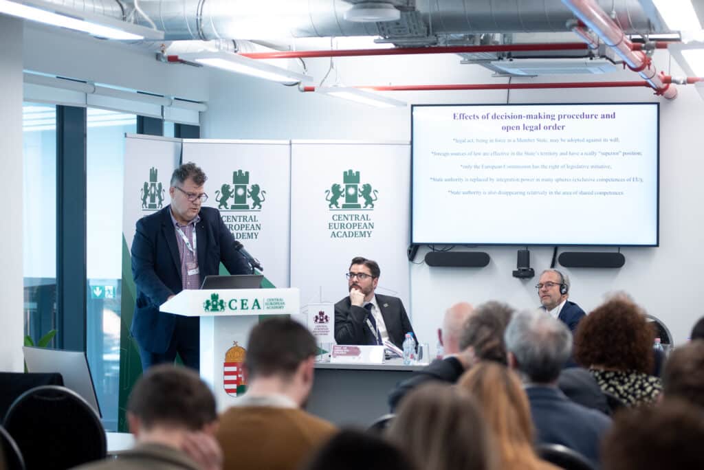Előadó férfi prezentál a CEA pódiumán, háttérben kivetítővel