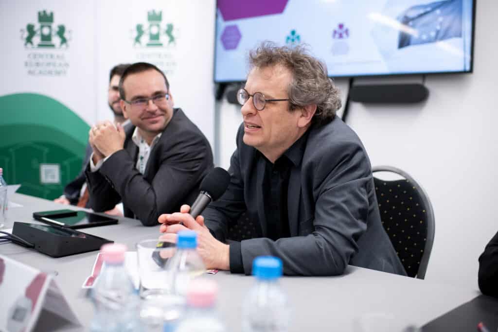 Előadó férfi prezentál a CEA pódiumán, háttérben kivetítővel