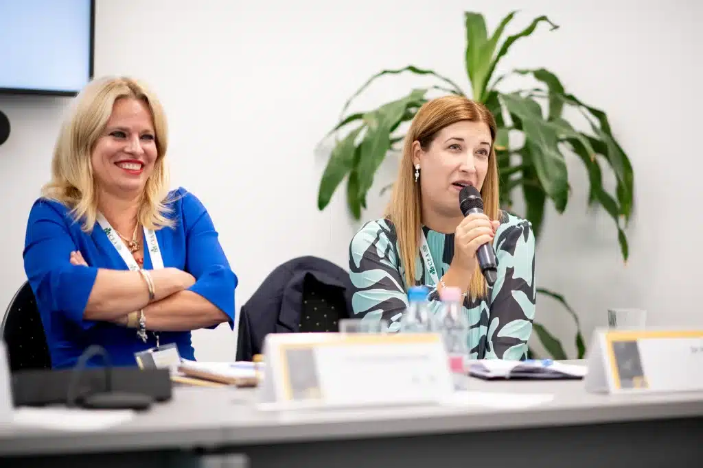 Female speaker smiling while presenting at the conference podium.