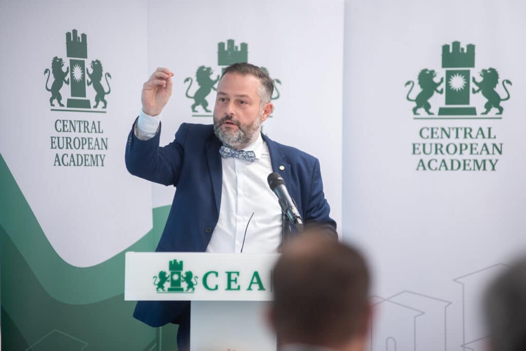Férfi előadó beszédet tart a Central European Academy logója előtt