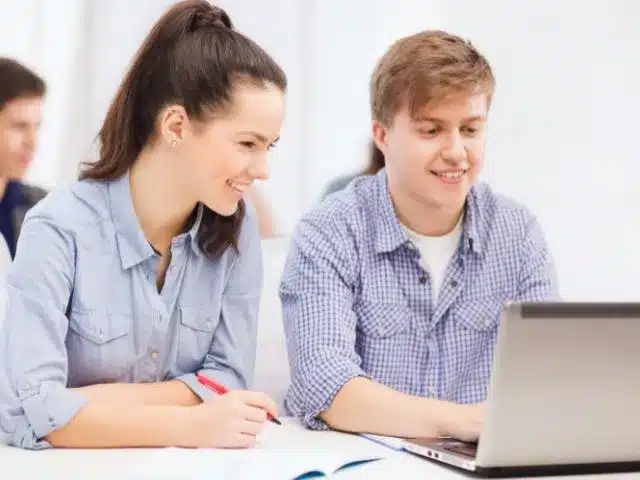 Fiatal férfi és nő együtt dolgoznak egy laptopon, mosolyogva.