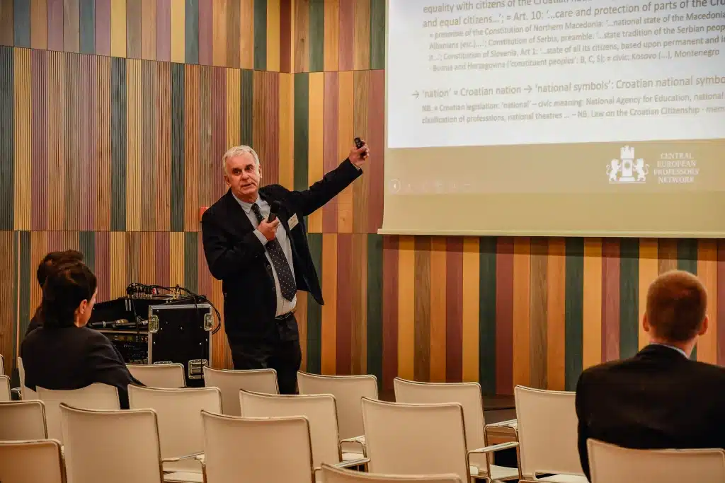 Male presenter standing in front of audience with screen