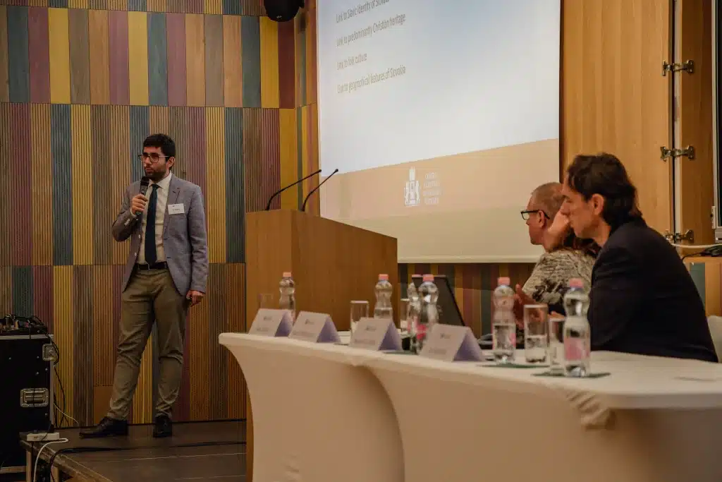 Male presenter standing in front of audience with screen