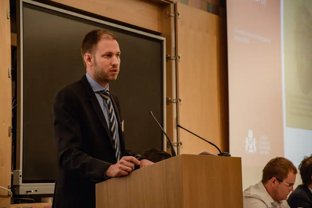 Male presenter standing in front of audience with screen