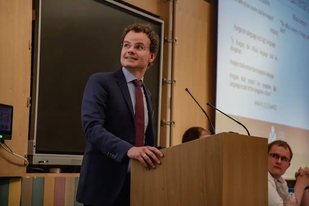 Male presenter standing in front of audience with screen