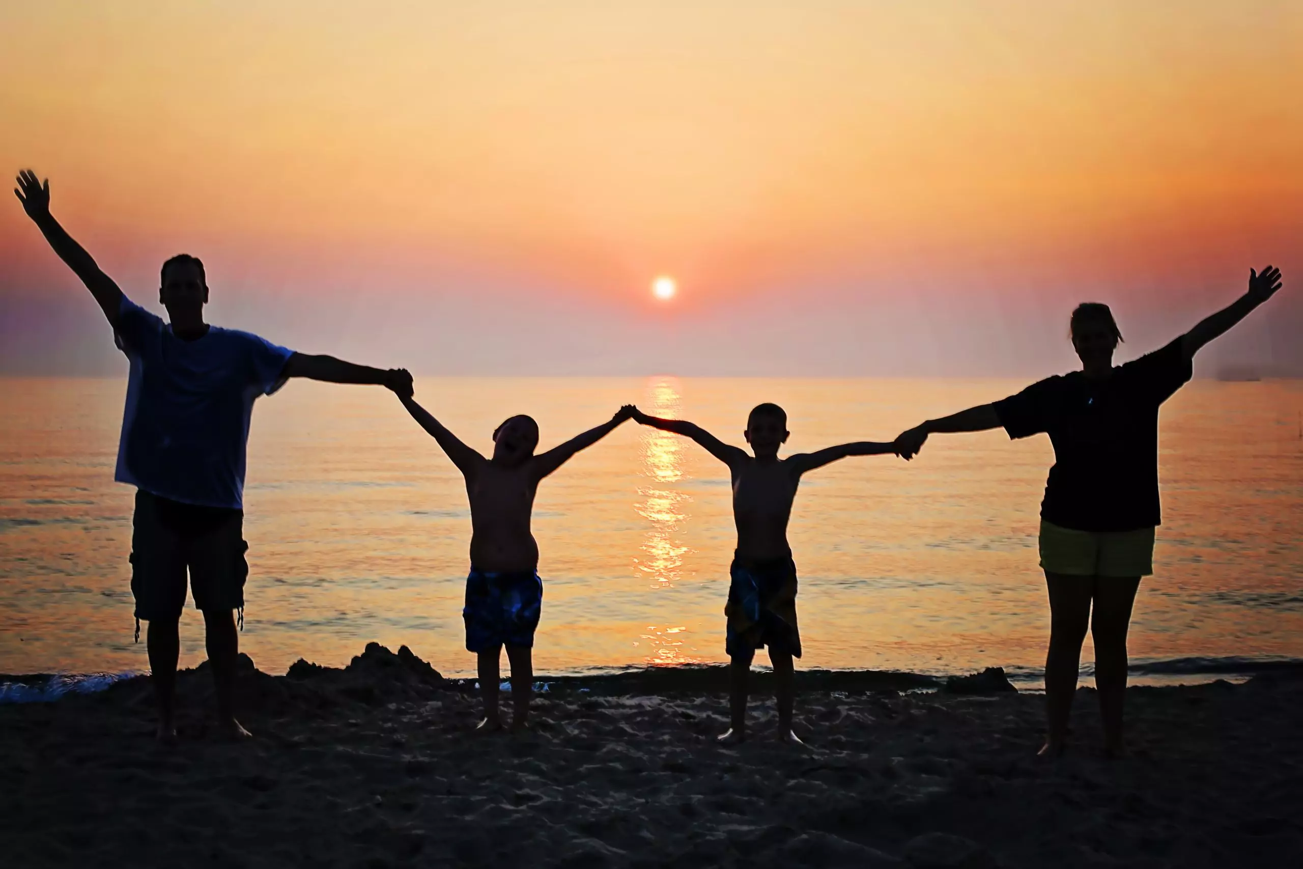 Family holding hands on the beach at sunset with arms outstretched.