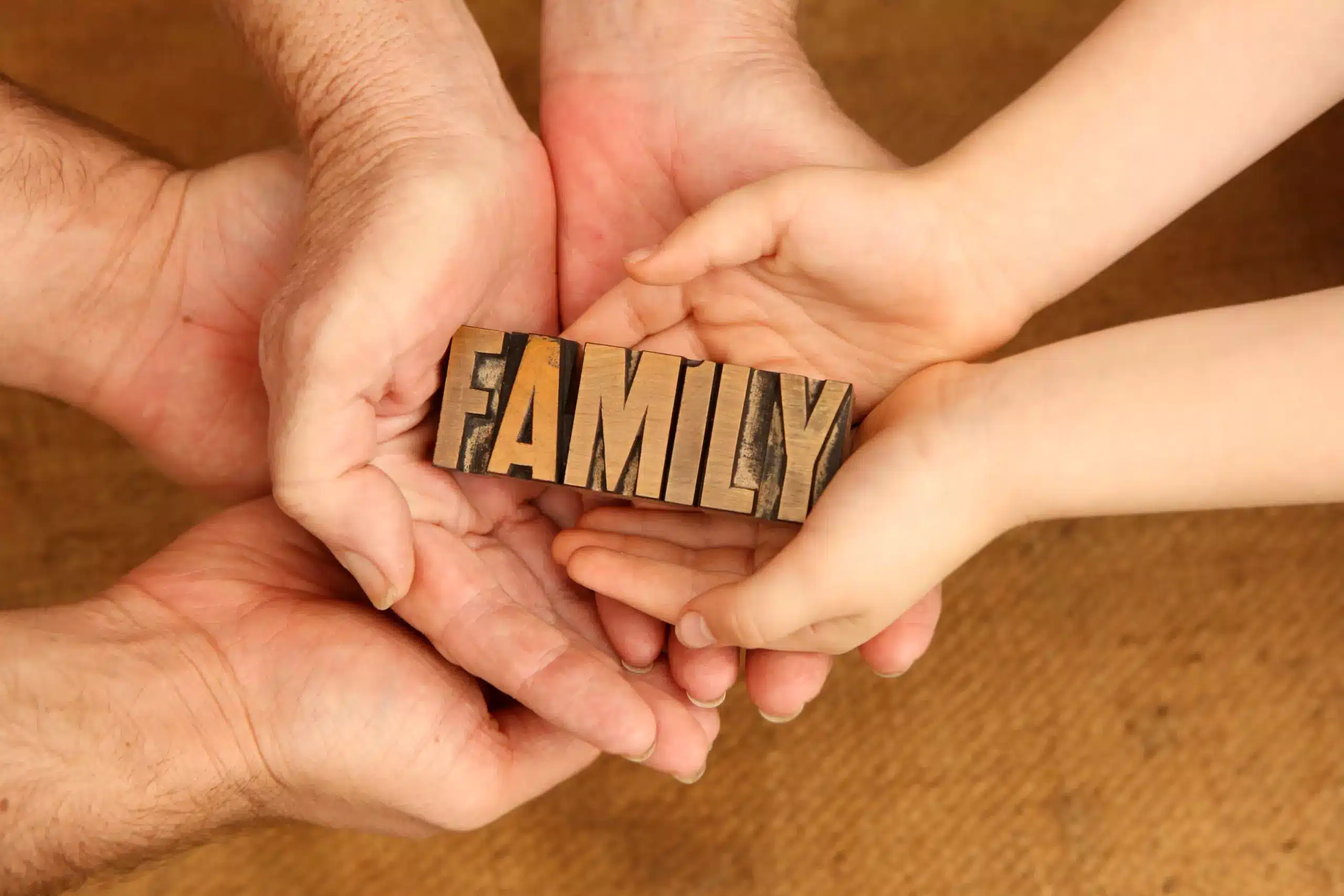 Child and adult hands holding together the word FAMILY, symbolizing family unity.