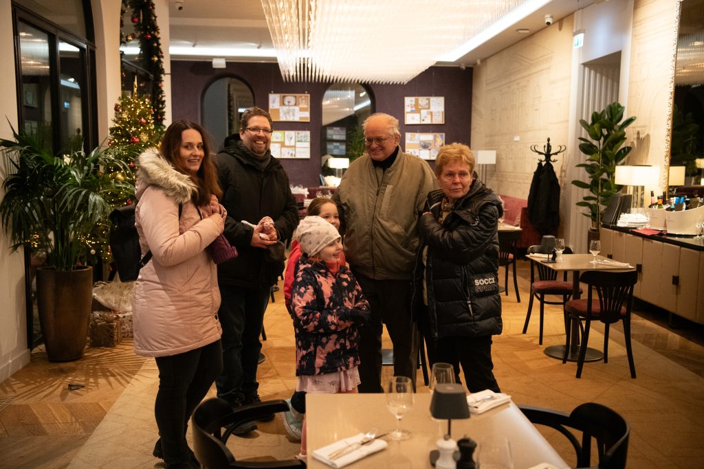 Család mosolyogva áll a kávézó belsejében.