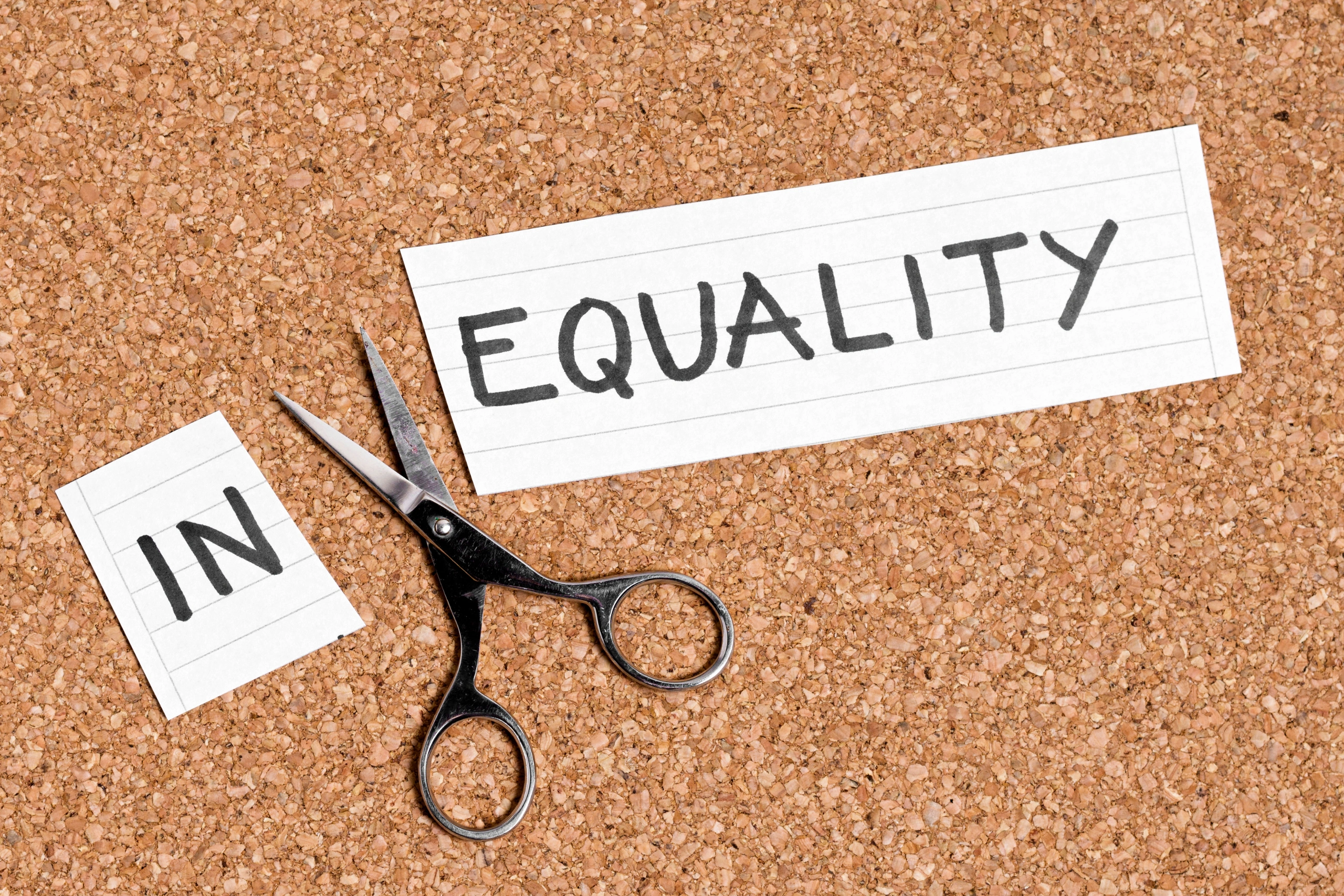 Scissors cutting the word "Equality" on a corkboard