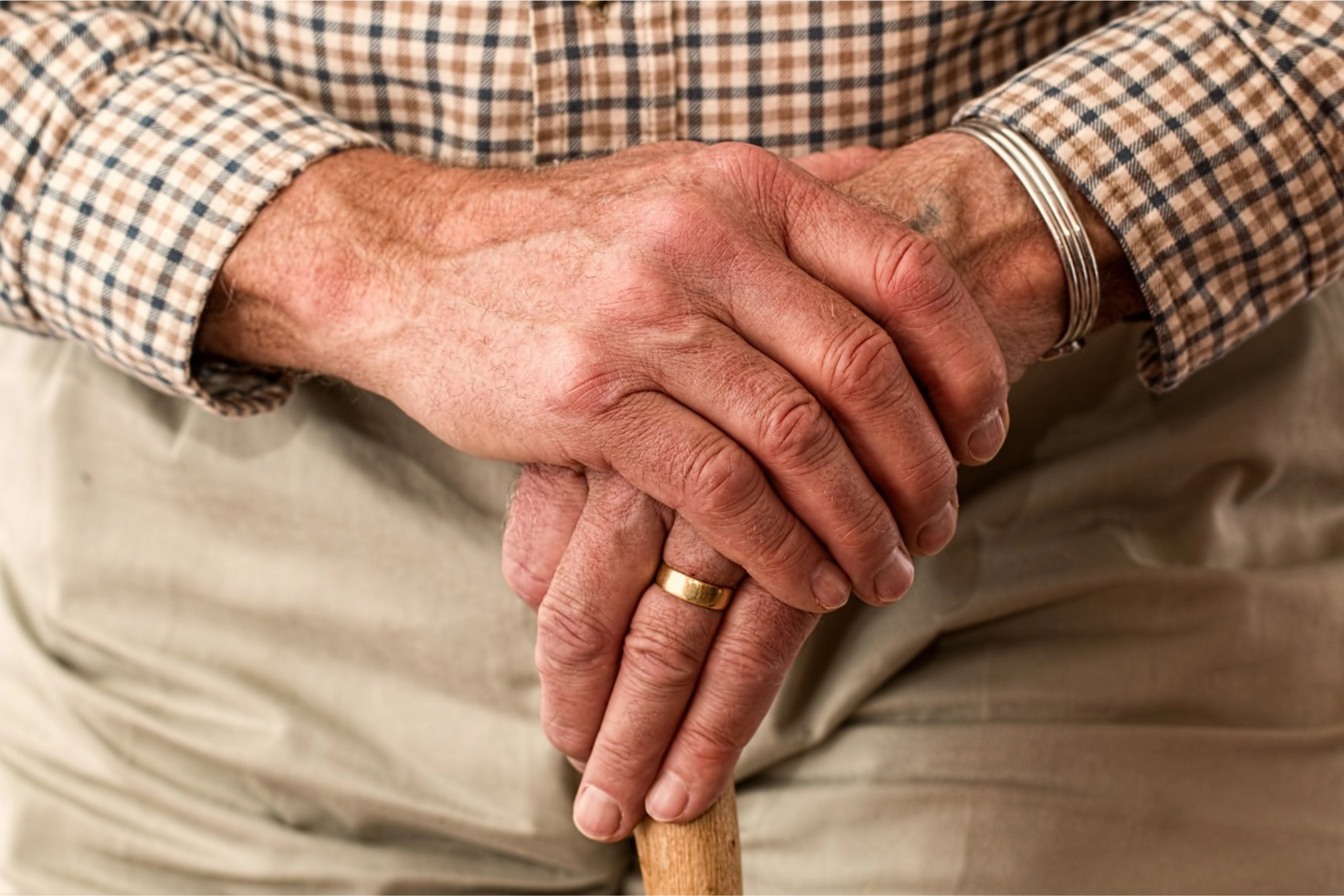 Elderly man with clasped hands leaning on a cane
